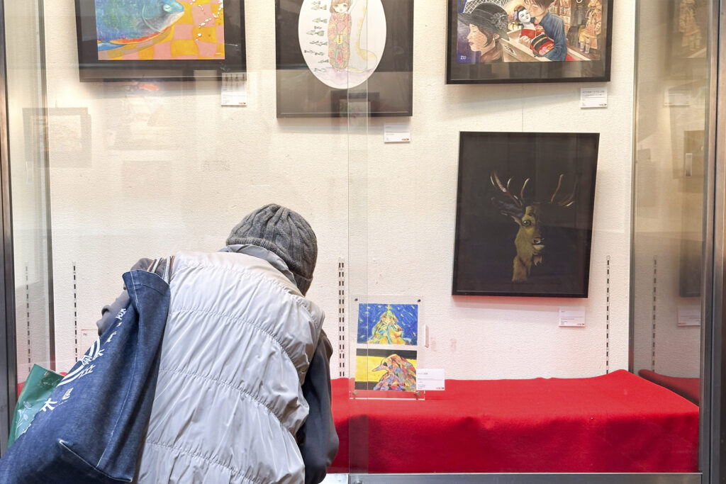 昨年の展示風景。女性がガラス越しに絵画を見ている